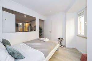 A bedroom with a bed, a large mirror, a door leading to a bathroom, and a window.