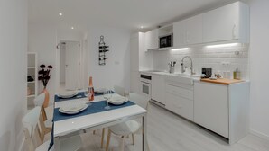 A modern kitchen with white cabinets, a built-in microwave, and a dining area with a table set for two. - Suprema loft l (Lisboa)