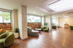 A spacious lobby with a wooden floor, green seating, a decorative column, and large windows. - Lasantel Bangkok (Bang Sao Thong)