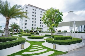 A hotel courtyard with manicured hedges, a palm tree, and a modern building in the background. - Lasantel Bangkok (Bang Sao Thong)