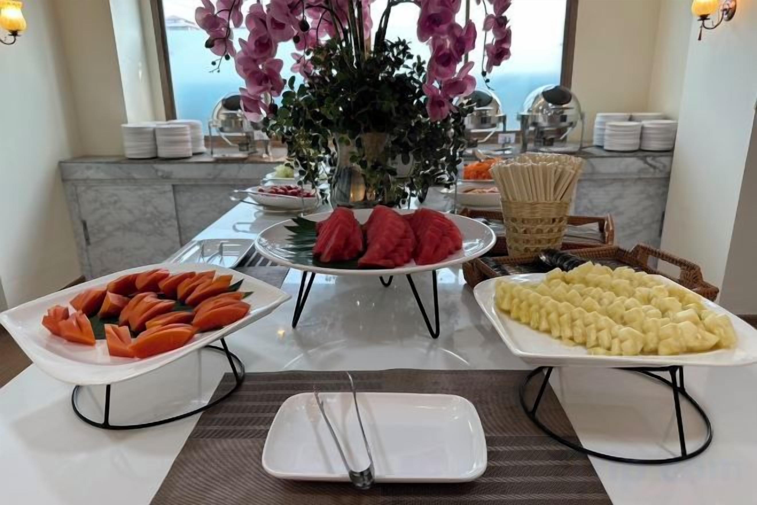 Een buffet met diverse gerechten, een bloevas en een uitzicht op zee door een raam.
