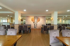 A spacious dining area with multiple tables and chairs, a central mural, and a modern interior design.