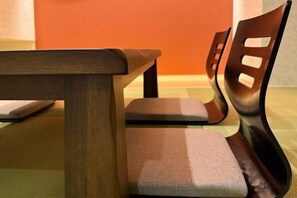 A wooden table with a cushioned bench in a room with a plain orange wall. - EI･GESSHO (Osaka)