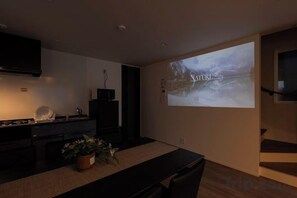 A modern living room with a flat-screen TV mounted on the wall, a dining table, and a staircase to the right. - EI･GESSHO (Osaka)