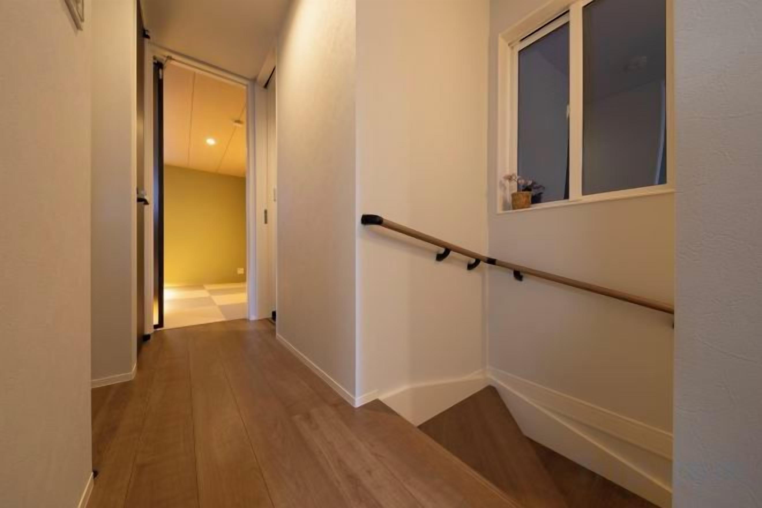 A narrow hallway with wooden flooring, a handrail on the right, and a door leading to another room.