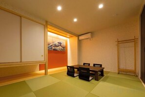 A room with tatami flooring, a low table with chairs, a sliding door, and a wall-mounted air conditioner. - EI･GESSHO (Osaka)
