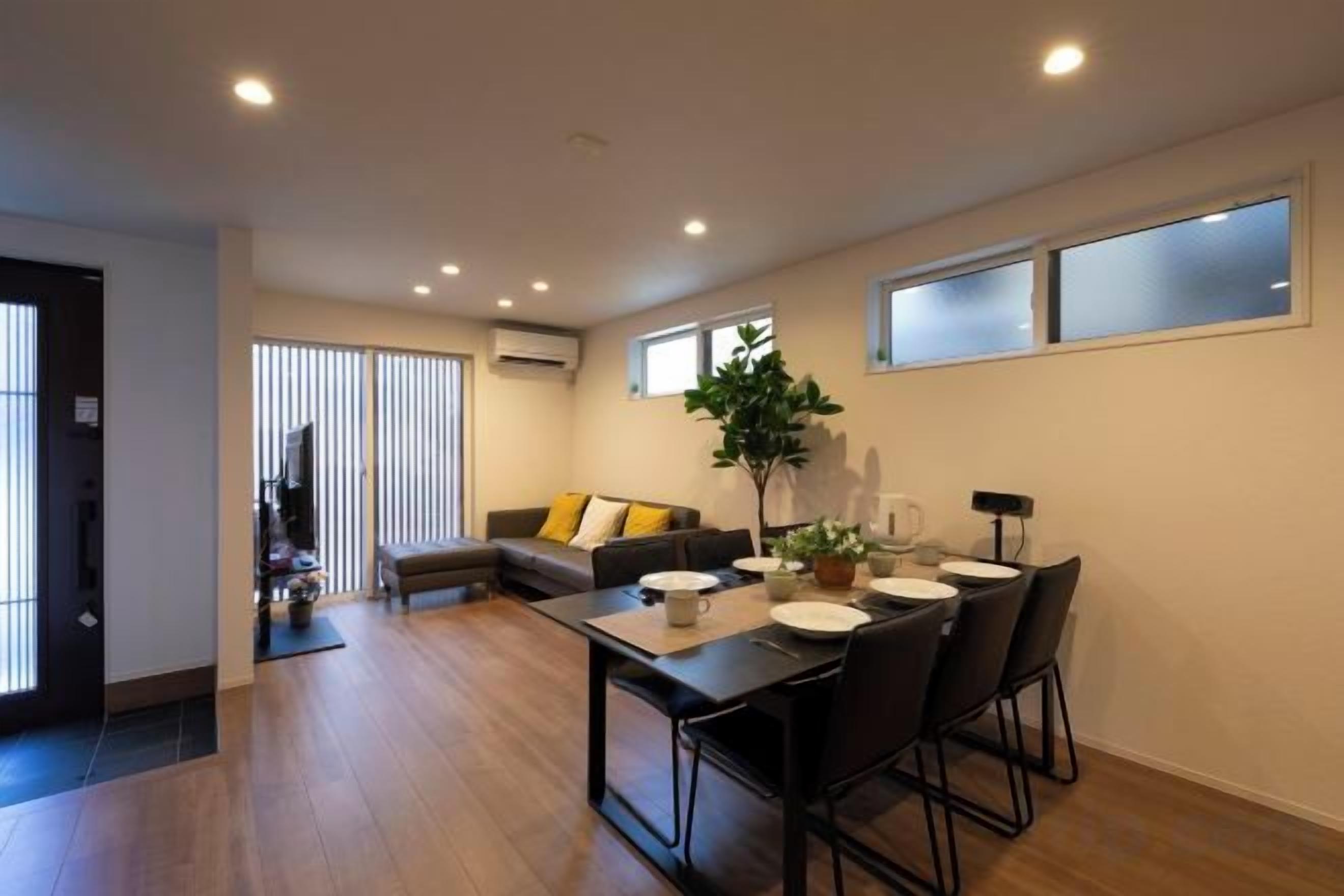 A modern living room with a sofa, a dining table with chairs, and a large window.