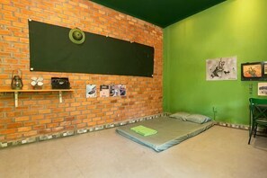 Ein Zimmer mit Ziegelwand, grüner Wand, einem Bett, einem Stuhl und einigen Kunstwerken.