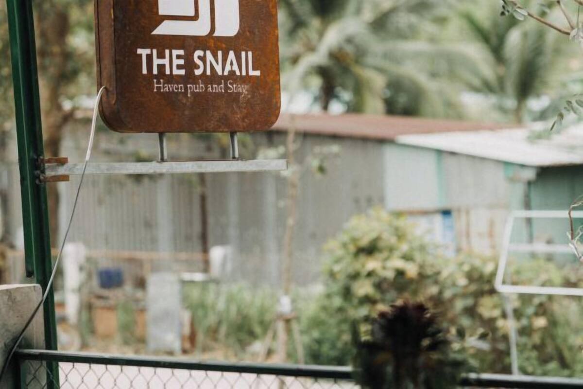 A sign for 'The Snail Haven pub and stay' with a rustic metal sign and a chain-link fence in the background.