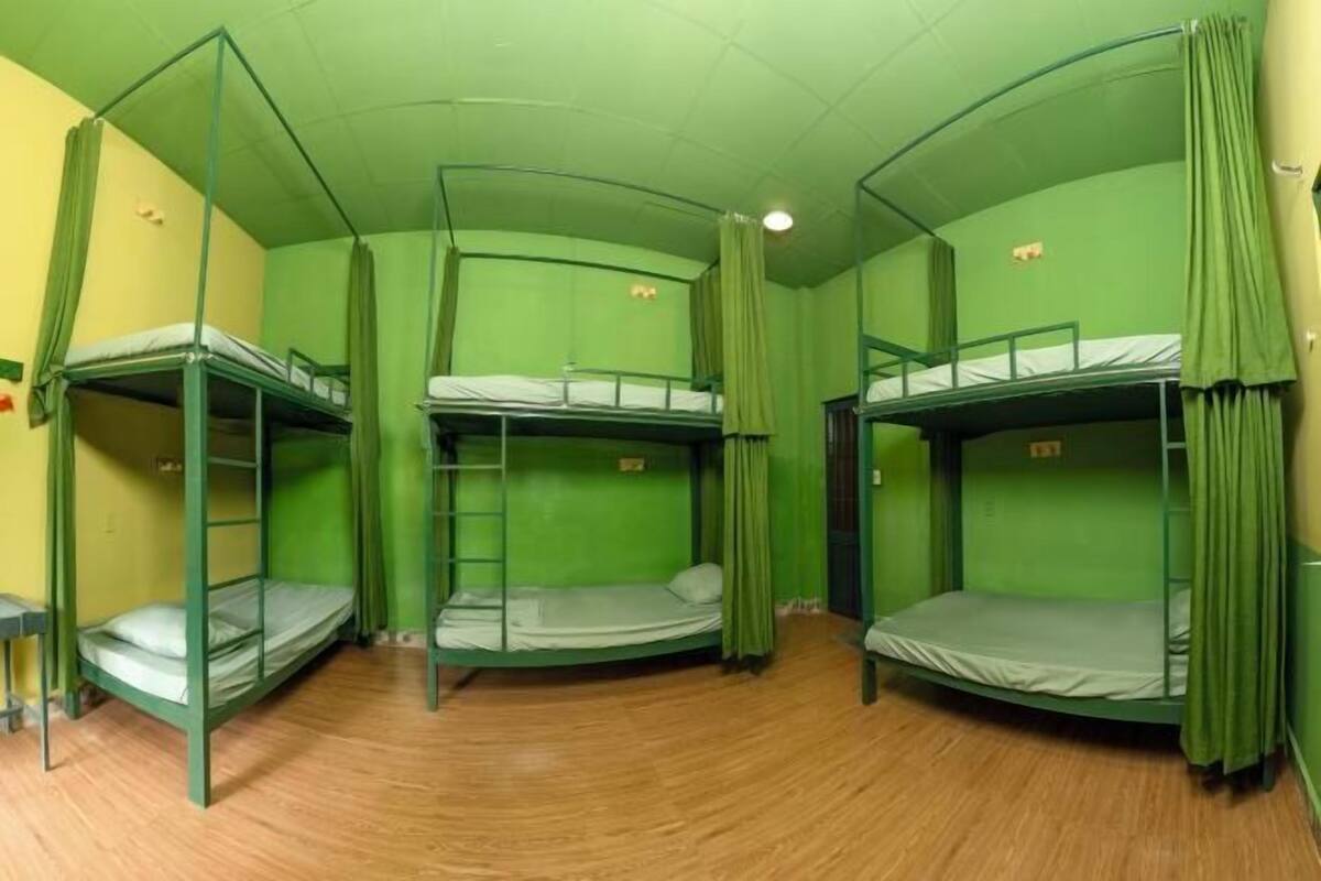 A room with bunk beds, green curtains, and a wooden floor.