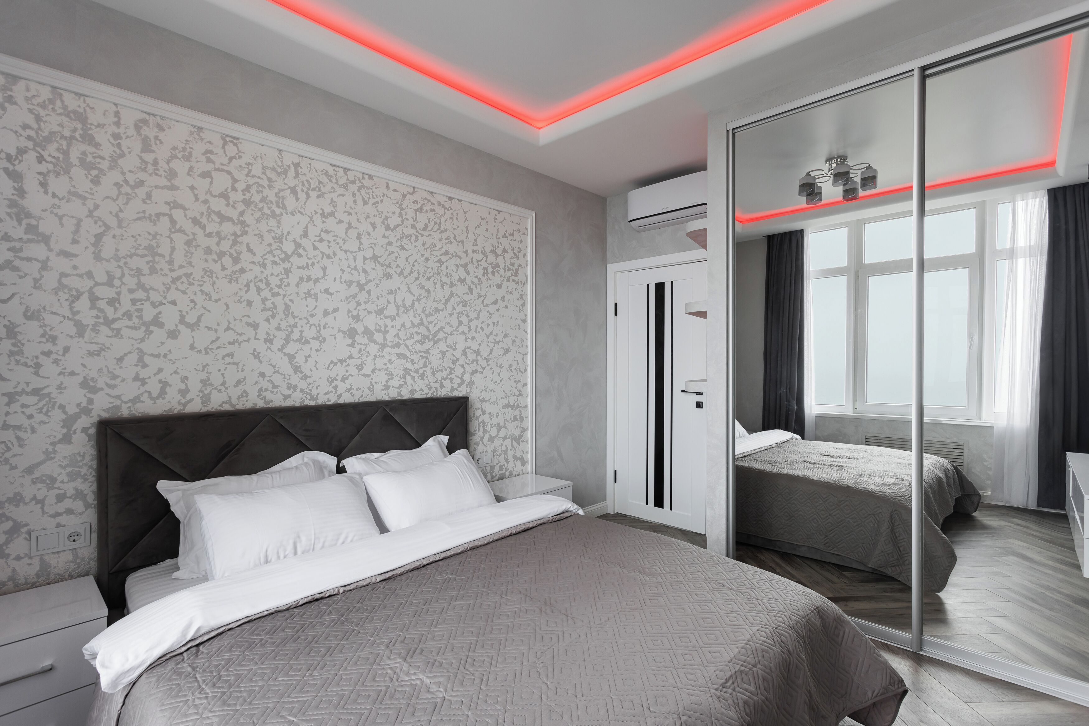 A modern bedroom with a large bed, a wardrobe, and a mirror.