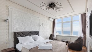 Una habitación de hotel moderna con una cama grande, vista al mar, una lámpara de techo original y un rincón de descanso acogedor.