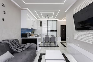 Een moderne woonkamer met een grijze bank, een witte salontafel en een tv die aan een bakstenen muur is bevestigd.