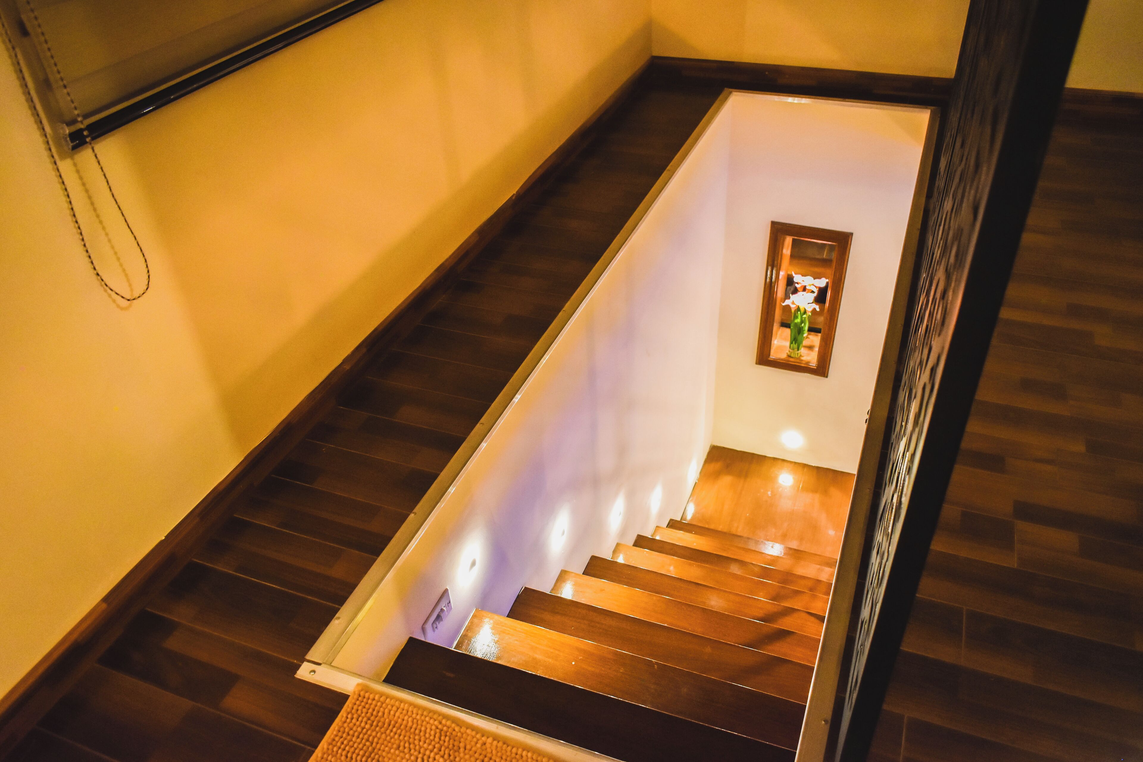 Un escalier avec des marches en bois et une rampe, menant à un palier où est accrochée une image encadrée.