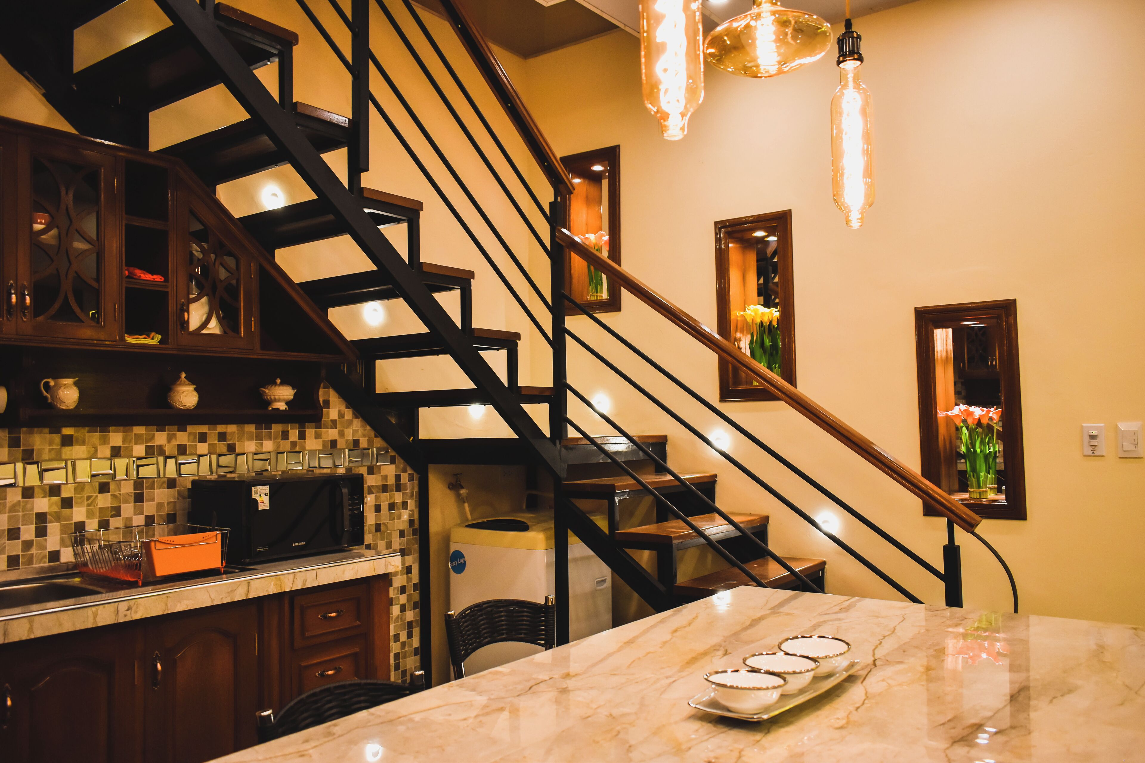 A kitchen with a marble countertop, a built-in microwave, and a staircase with a wooden railing.