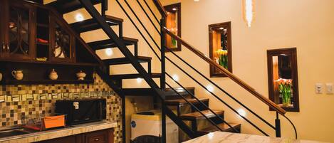 A kitchen with a marble countertop, a built-in microwave, and a staircase with a wooden railing.