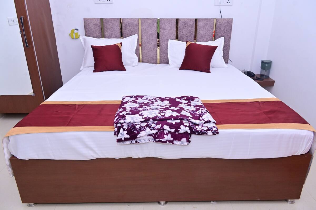 A neatly made bed with white and maroon bedding, a floral throw blanket, and a wooden headboard.