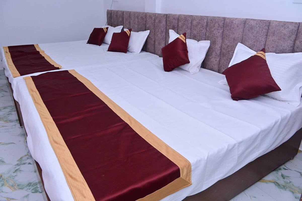 A double bed with a white and maroon bedspread, multiple pillows, and a headboard.