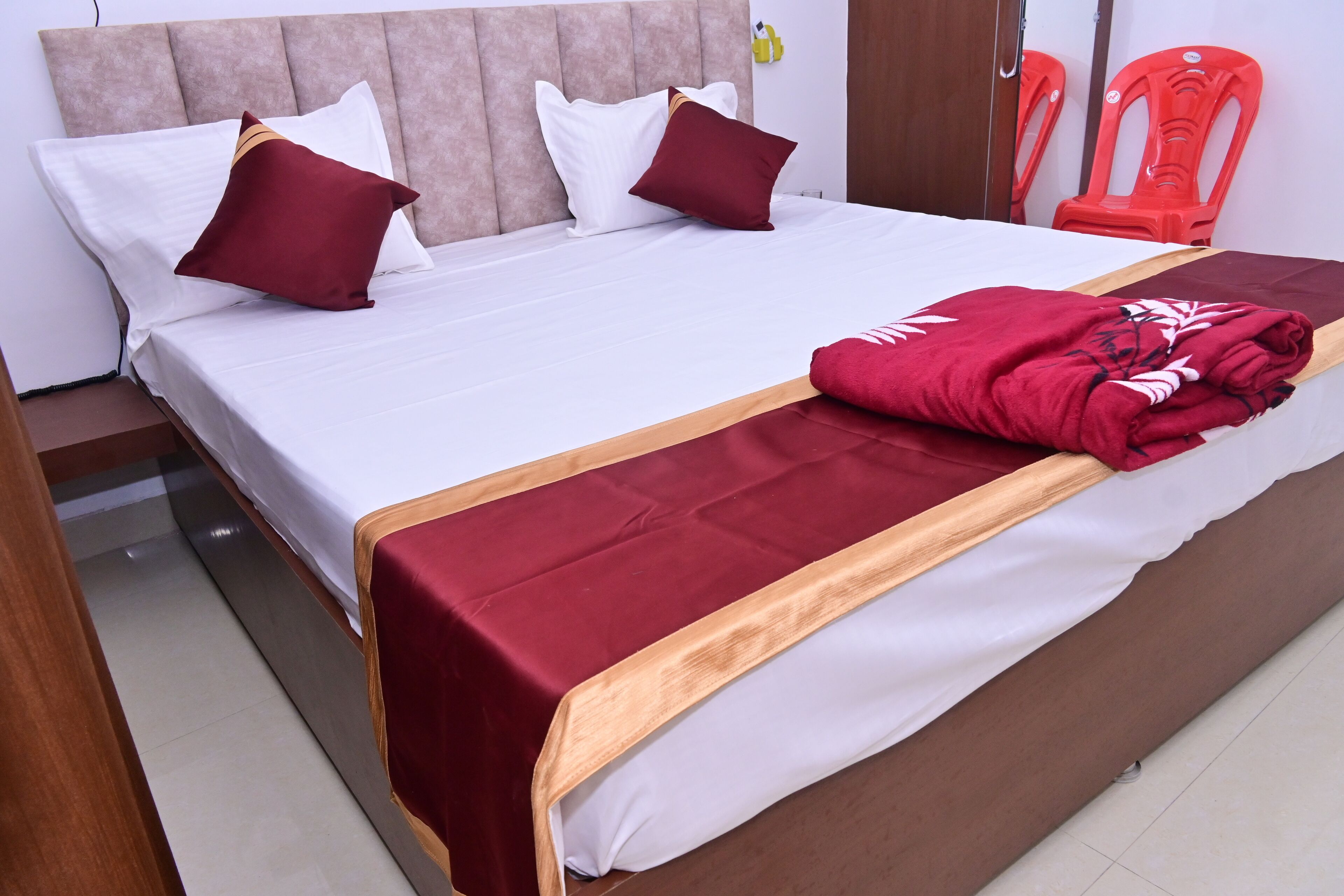 Un lit bien fait, recouvert d’une couvre-lit blanche et bordeaux, avec une tête de lit en bois et un plaid rouge.