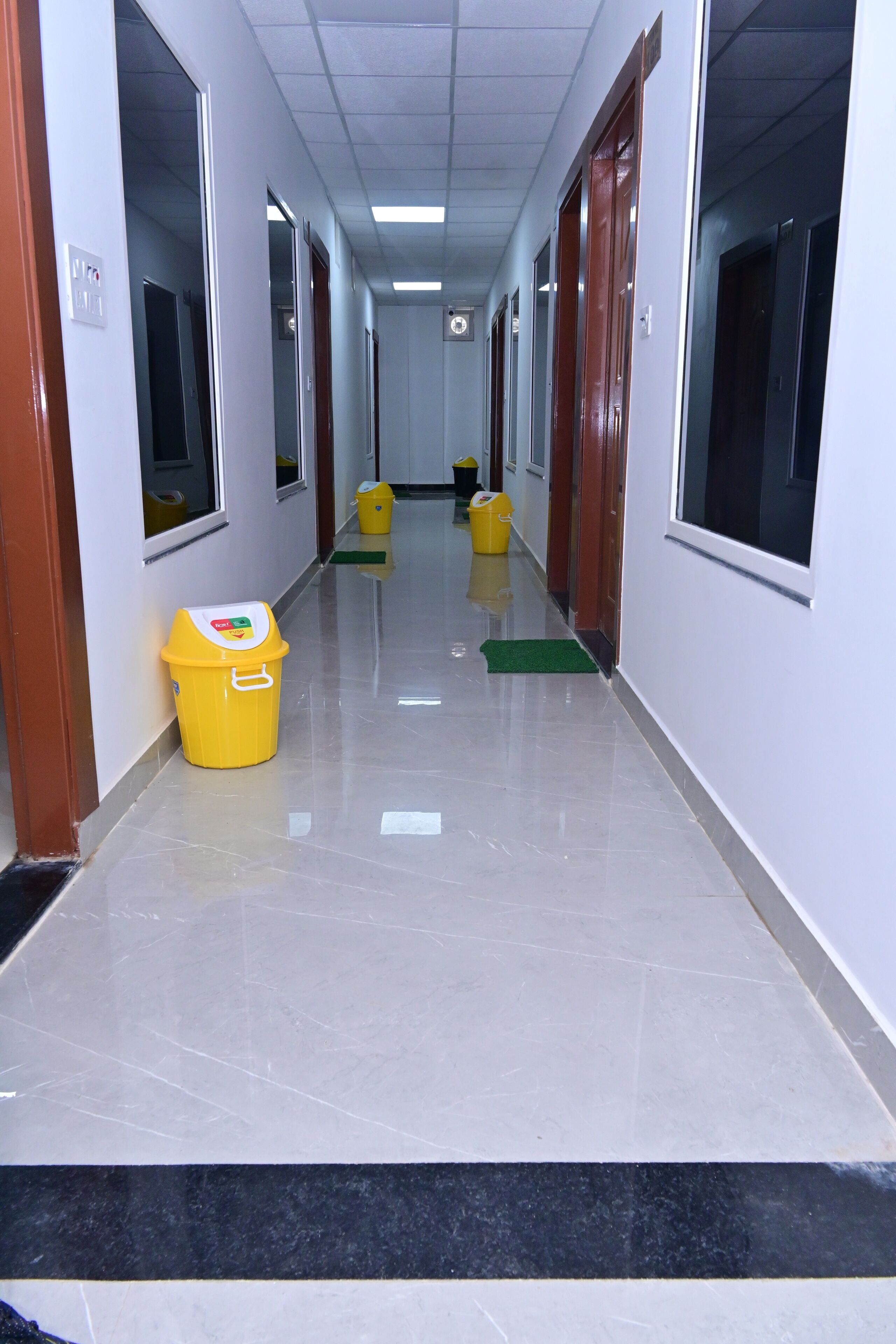 A hallway with a yellow trash bin, a green mat, and a yellow bucket.