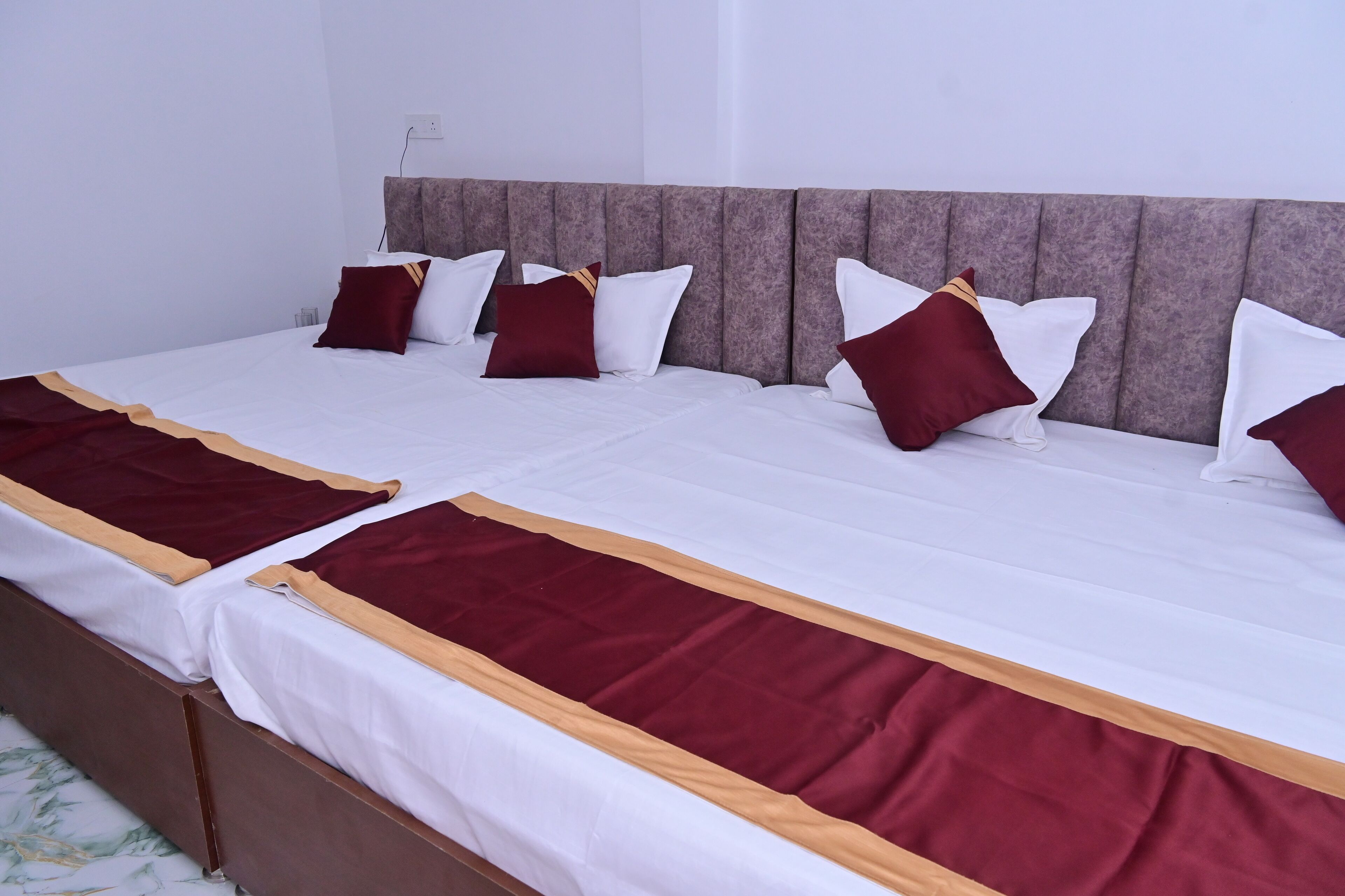 A double bed with white and maroon bedding, a wooden headboard, and a marble-patterned wall.