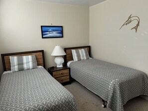 A hotel room with two beds, a nightstand, a lamp, a framed picture on the wall, and a decorative fish on the wall.