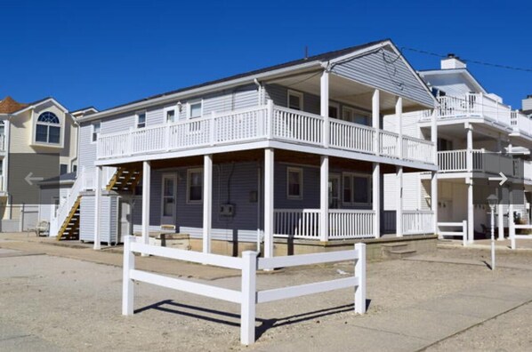 A beachfront house with a balcony, a covered porch, and a staircase leading to the upper level.