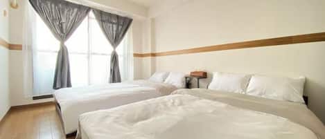 Habitación de hotel con dos camas, piso de madera, ventana con cortinas y mesita de noche con lámpara.