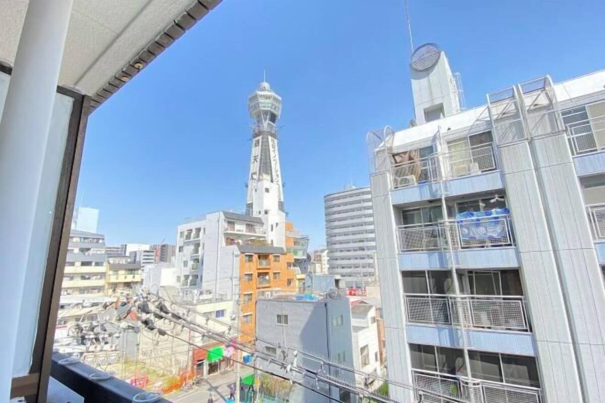 Un edificio alto con una torre destacada, una estructura moderna con balcones y un cielo despejado.