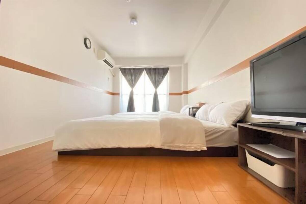 Habitación de hotel con cama, televisor y ventana con cortinas.