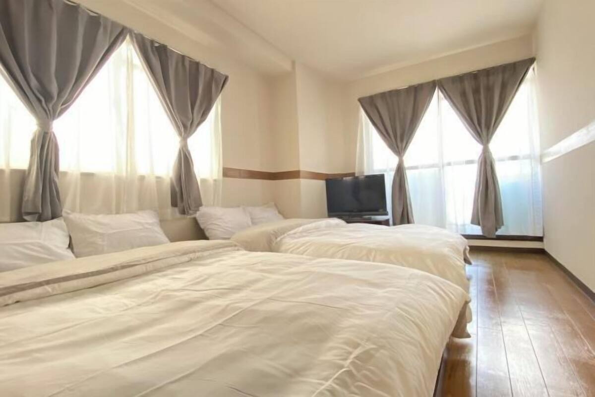 Habitación de hotel con dos camas, un televisor y ventanas amplias con cortinas.
