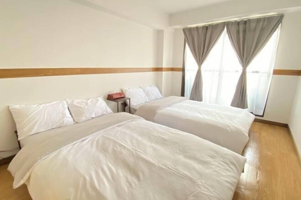 Habitación de hotel con dos camas, piso de madera y una ventana con cortinas.