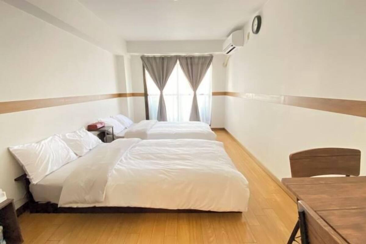 Habitación de hotel con dos camas, suelo de madera, una mesa de madera y una ventana con cortinas.