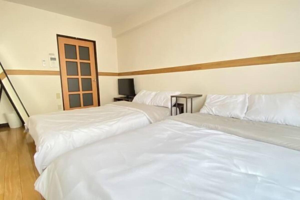 Habitación de hotel con dos camas, una puerta de madera, una mesita pequeña y un televisor.