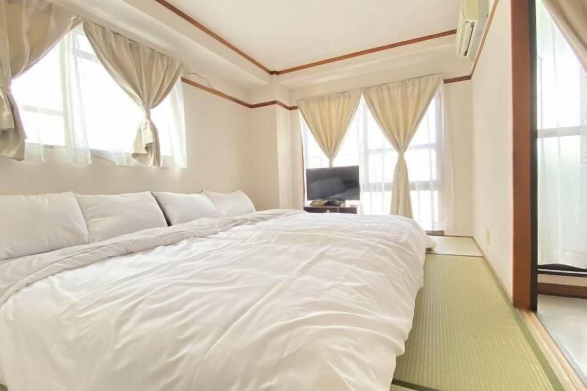 Habitación de hotel con una cama grande, un televisor sobre una mesita auxiliar y vistas al exterior por la ventana.