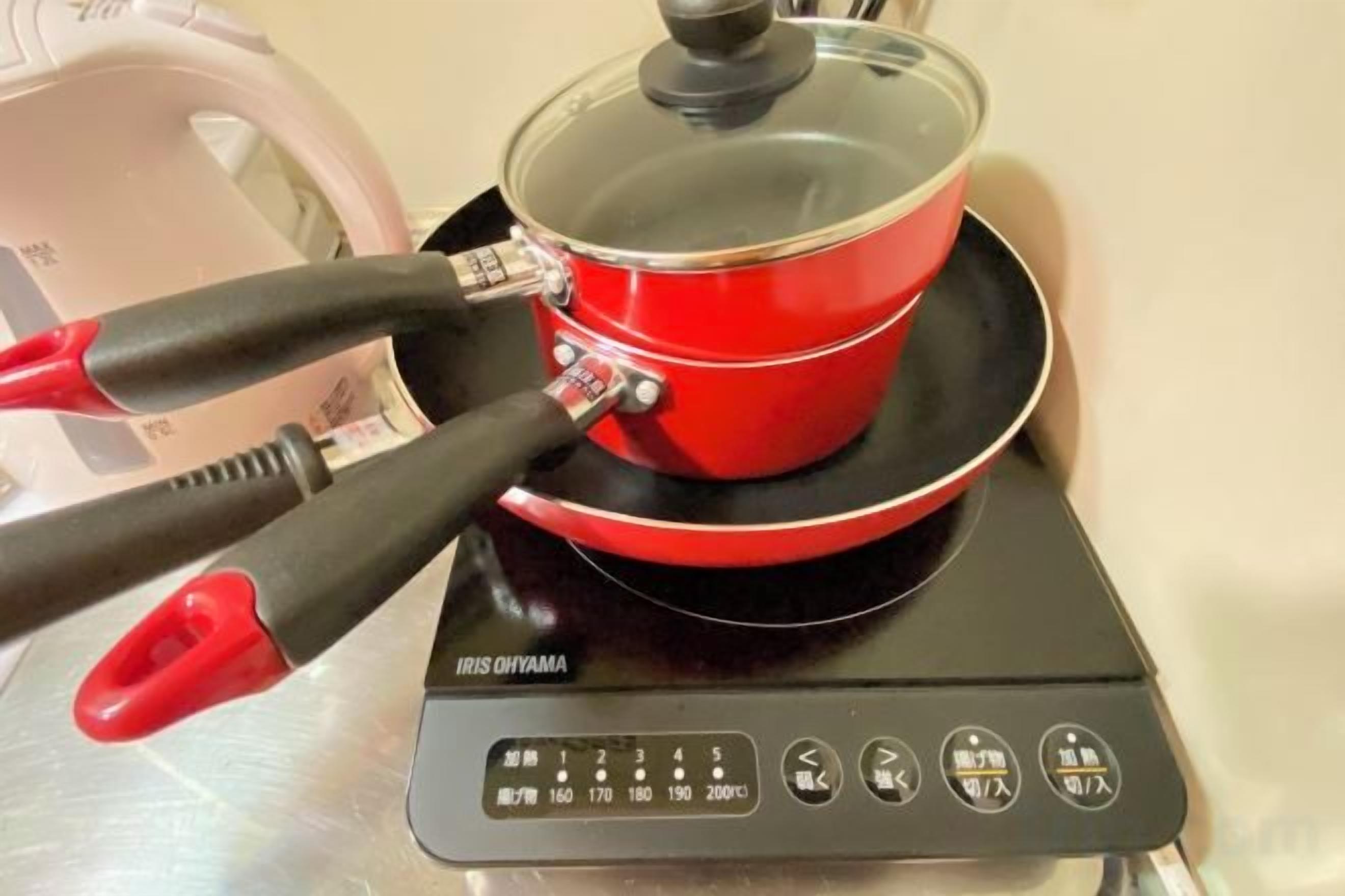 A red induction cooktop with a pot on it, connected to a power strip.