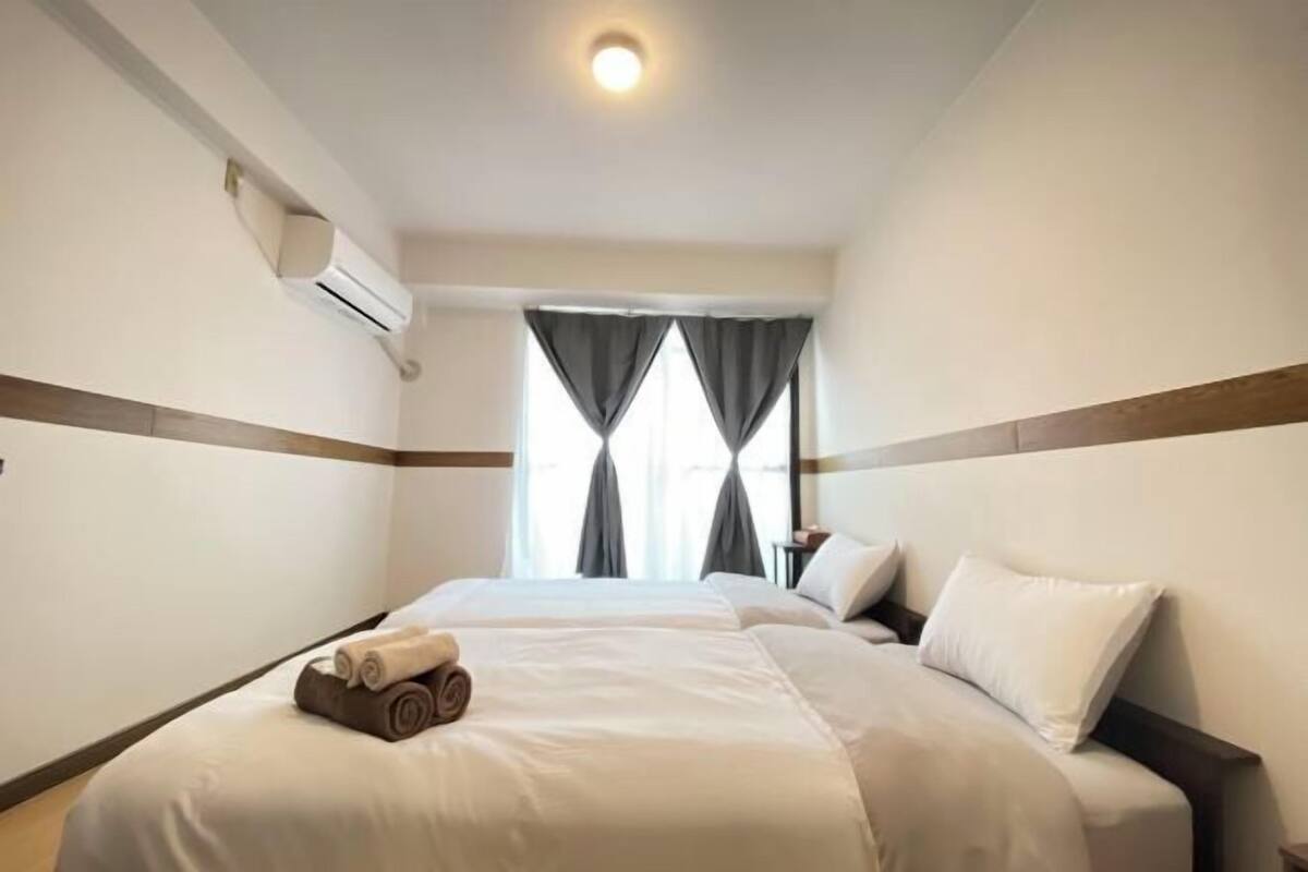 Habitación de hotel con dos camas, una ventana con cortinas, un equipo de aire acondicionado y una mesita de noche.