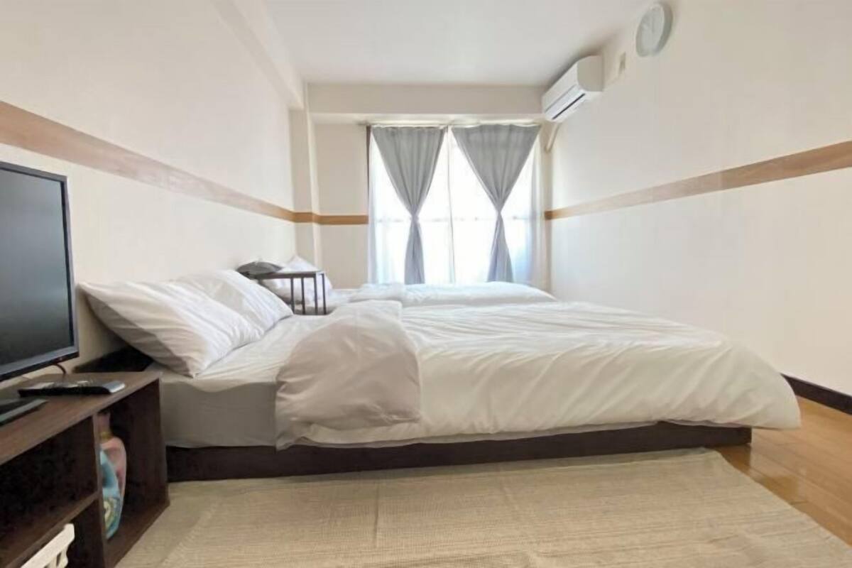 Habitación de hotel con cama, televisor en un mueble, ventana con cortinas y aire acondicionado.
