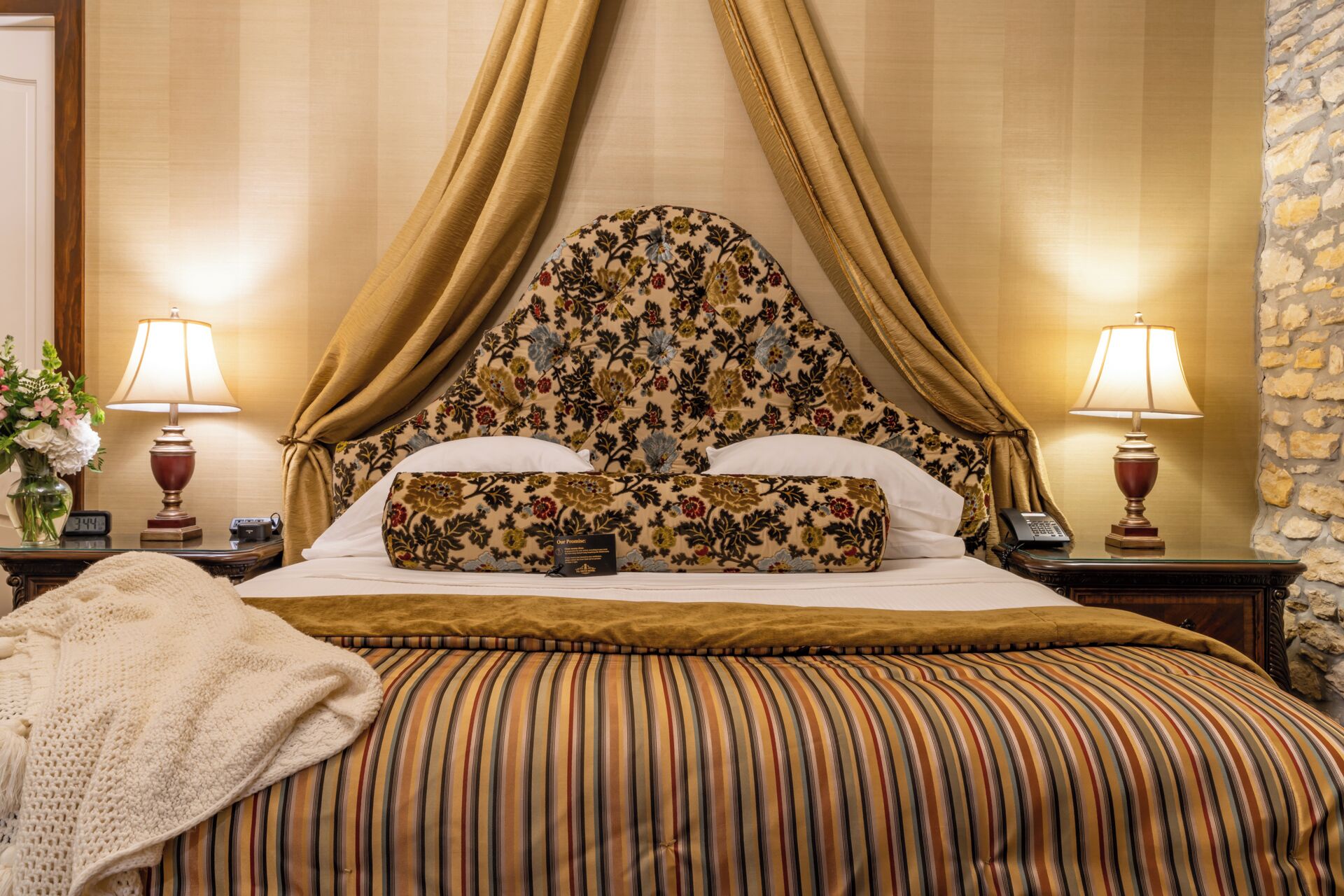 A hotel room with a canopy bed, floral headboard, striped bedding, and two bedside lamps.
