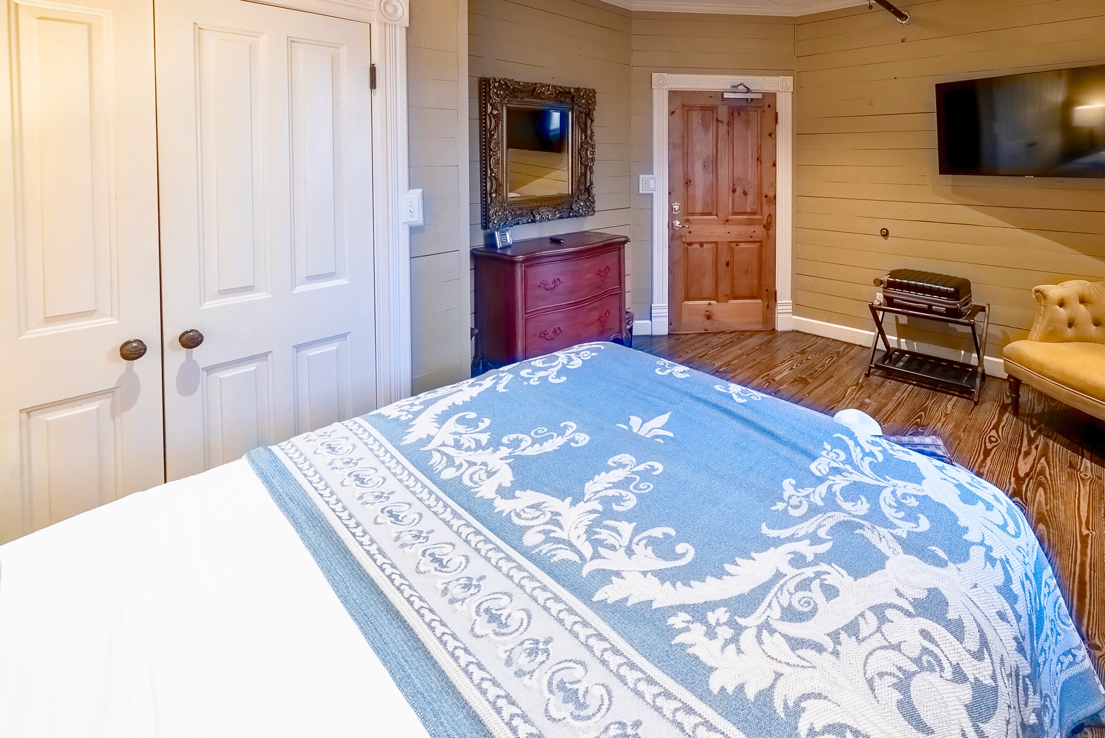 A bedroom with a bed, a dresser, a mirror, a TV, and a chair.