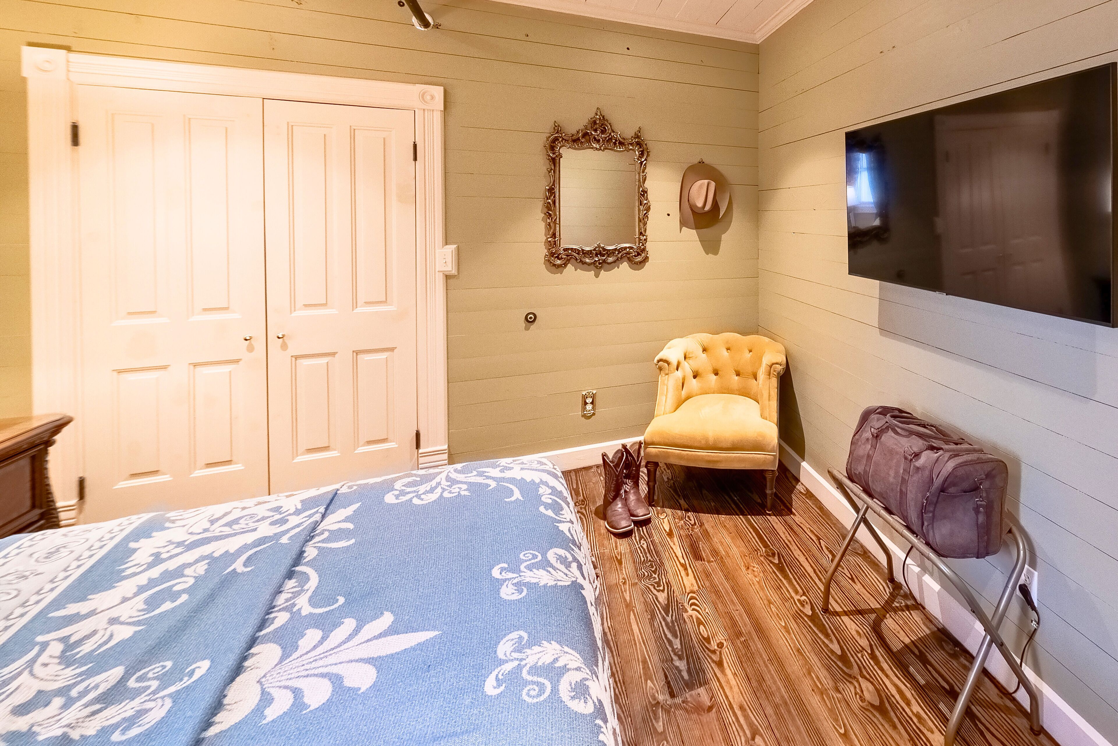 A bedroom with a bed, a chair, a mirror, a wardrobe, and a TV.
