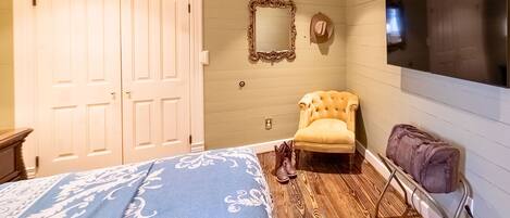 A bedroom with a bed, a chair, a mirror, a wardrobe, and a TV.