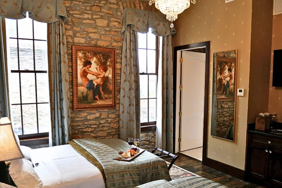 A hotel room with two beds, a stone wall, a large window, and a chandelier.