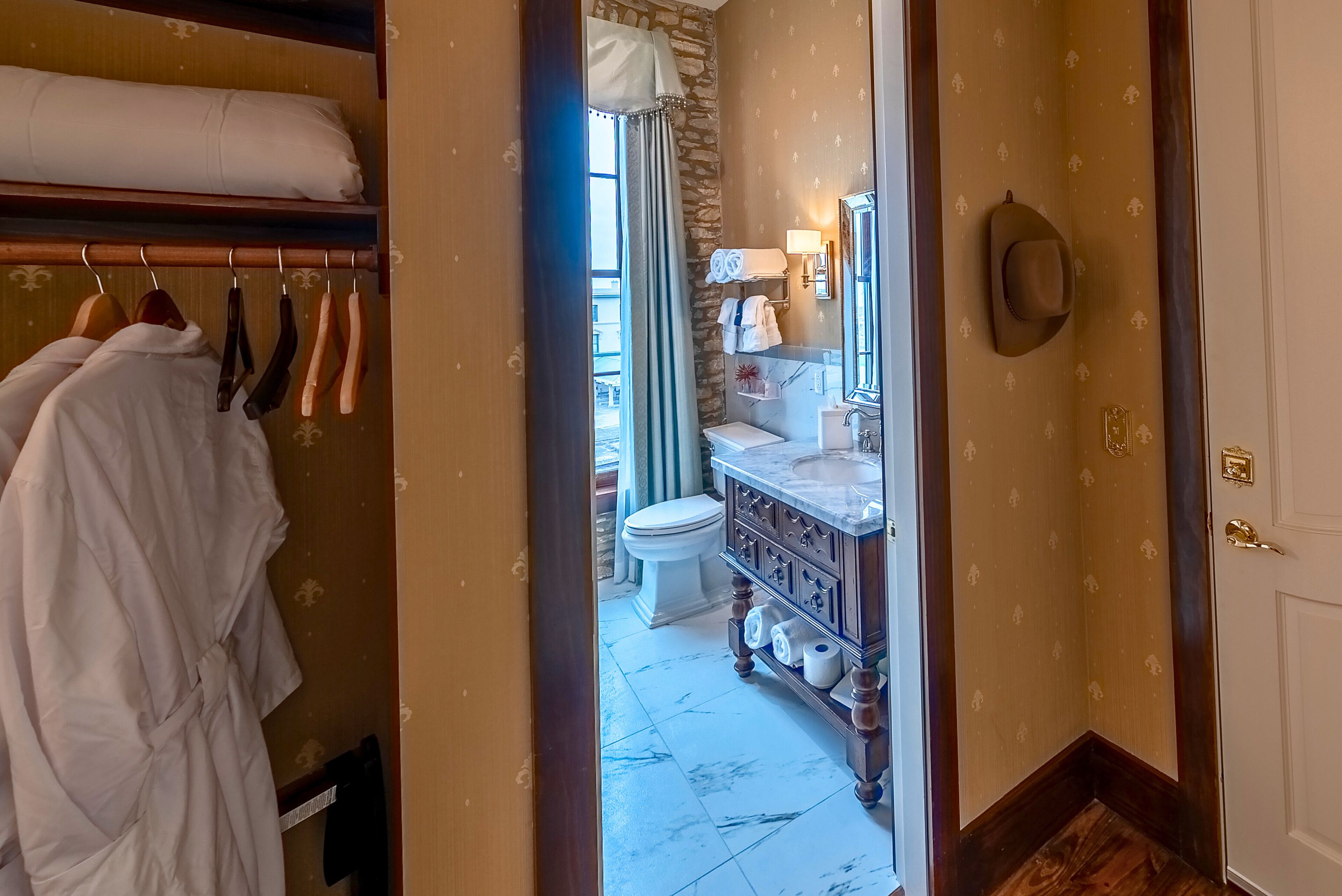 Un baño de hotel con piso de mármol, inodoro blanco y tocador con espejo y perchero.