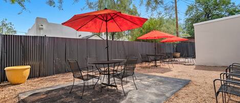 An outdoor patio area with metal tables and chairs, red umbrellas, and a yellow planter.