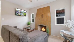 Ein Wohnzimmer mit Kamin, einer Couch, einem Fernseher und einem Deckenventilator.