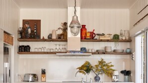A kitchen with white cabinetry, a central island with stools, hanging pendant lights, and various kitchen items on shelves.