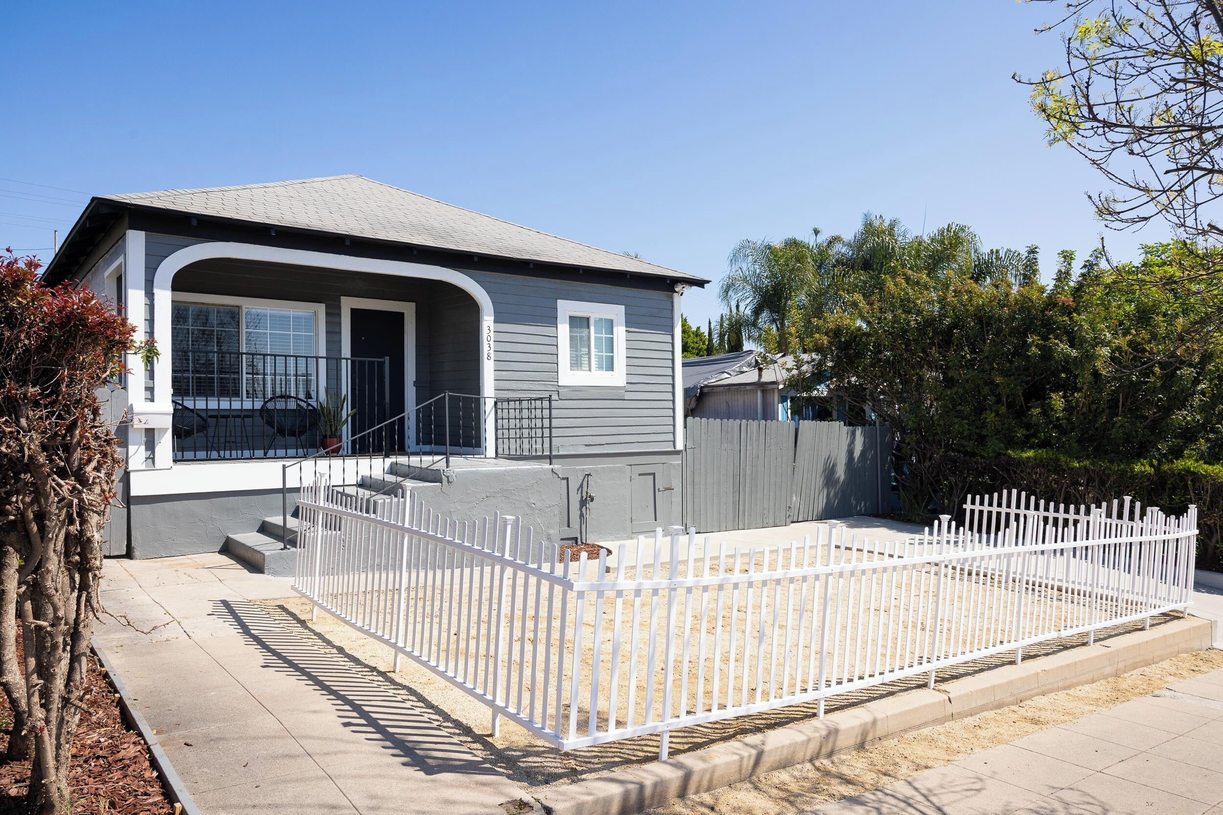 A single-story house with a grey exterior, a front porch, and a fenced backyard.