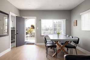 Un espace repas comprenant une grande table et des chaises, une fenêtre avec des stores et une porte donnant sur un espace extérieur.
