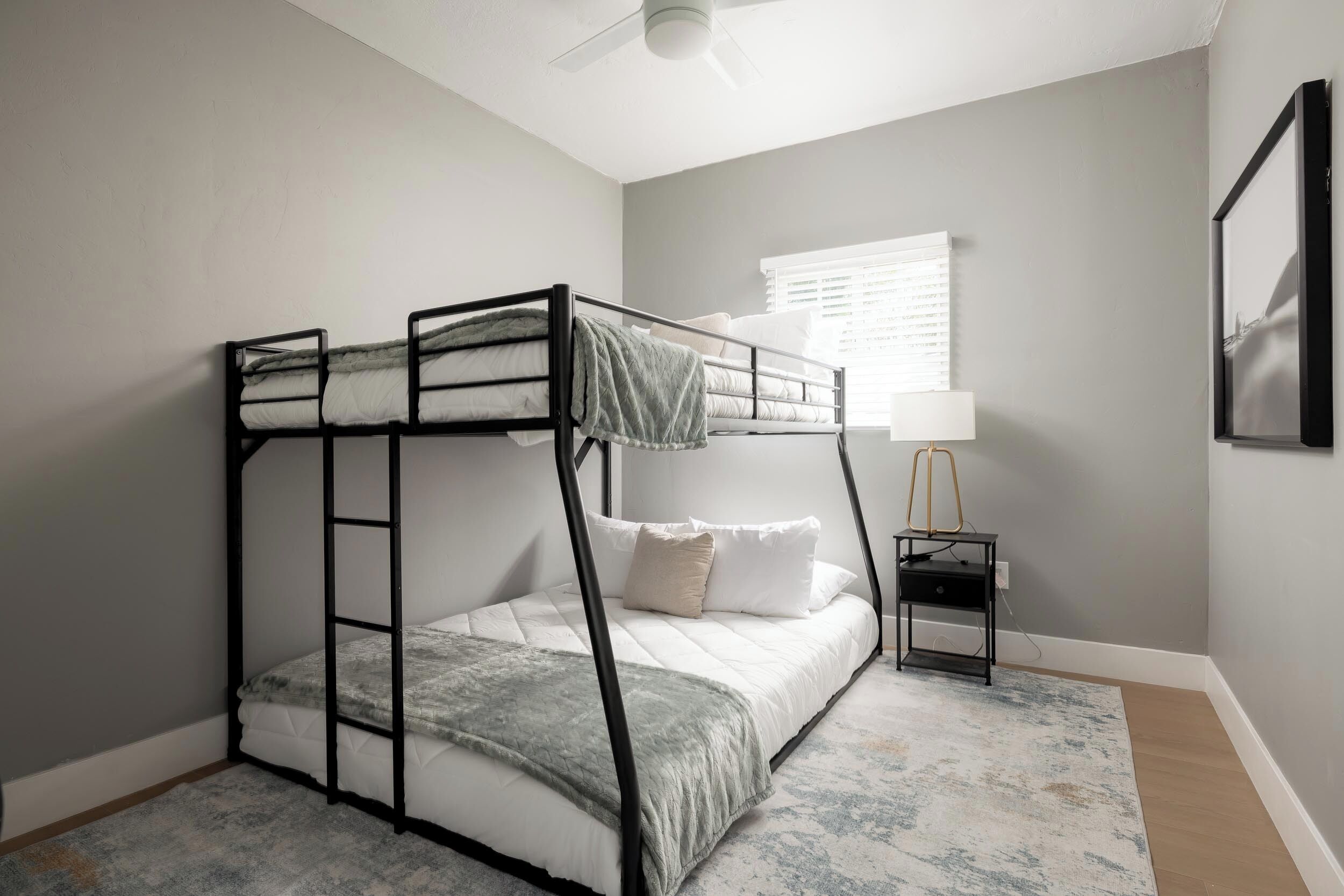 A bunk bed with a ladder, a bedside table with a lamp, and a window with blinds.